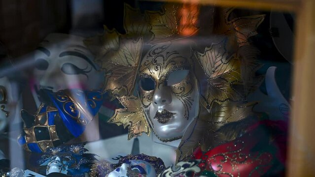 Beautiful Venetian Carnival Masks displayed in a shop in Venice with reflection of people passing by on the streets