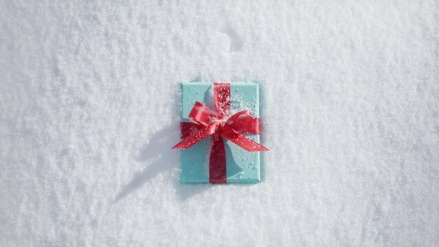 Cinematic still shot of elegant teal blue gift box with bright red satin ribbon laying on fresh snow surface on sunny winter day. Slow motion winter background shot on RED, Christmas gifts on December