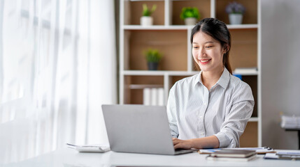 Young woman working on a laptop in the office. Asian businesswoman sitting at her workplace in the office.  Beautiful Freelancer Woman working online at her home. © crizzystudio