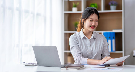 Young woman working on a laptop in the office. Asian businesswoman sitting at her workplace in the office.  Beautiful Freelancer Woman working online at her home.