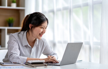 Asian woman freelancer is working her job on a laptop computer in a modern office. Doing accounting analysis report real estate investment data, Financial and tax systems concept.