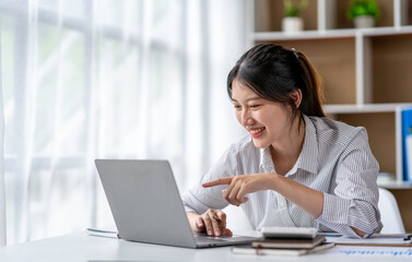 Asian woman freelancer is working her job on a laptop computer in a modern office. Doing accounting analysis report real estate investment data, Financial and tax systems concept.