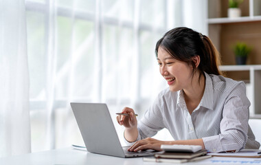 Asian woman freelancer is working her job on a laptop computer in a modern office. Doing accounting analysis report real estate investment data, Financial and tax systems concept.