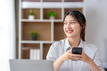 Positive asian young female accountant using a smartphone at her office desk. Woman relaxing on her mobile application.