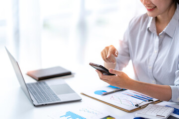 Positive asian young female accountant using a smartphone at her office desk. Woman relaxing on her mobile application.