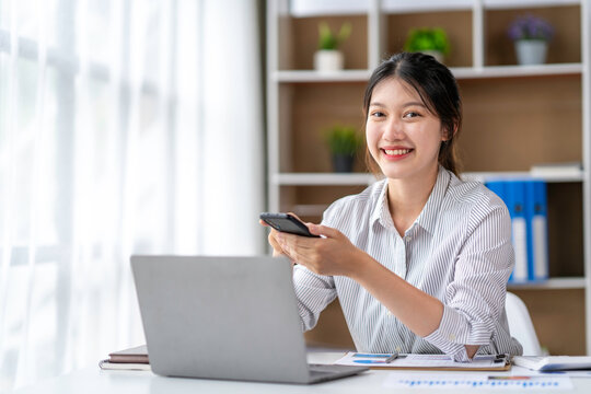 asian businesswoman smiling and look at camera while working on laptop at modern office. Woman laptop working concept