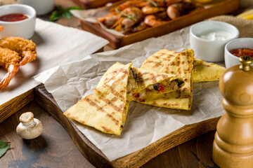 Quesadilla with chicken, sour cream and salsa sauces on the board, sliced, brown table