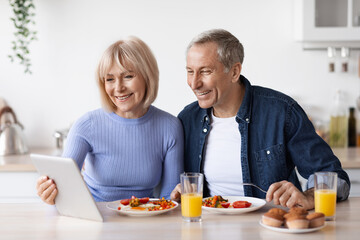 Happy senior couple using digital tablet while having breakfast