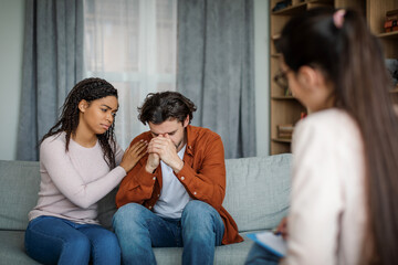 Sad millennial black lady calms european man at meeting with psychologist in office clinic...