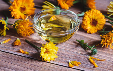Calendula officinalis cosmetic oil, dried and fresh marigold flowers on wooden table