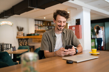 one caucasian man young adult millennial male using mobile phone sit at table in cafe at the table alone happy smile confident having online chat using internet for text messages or social network