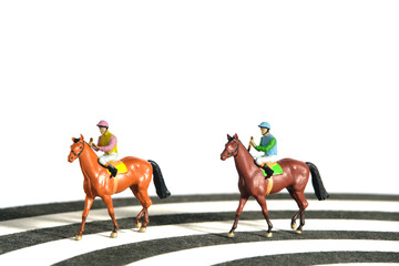Miniature people toy figure photography. Jockey men riding horse on a racetrack from dartboard. Isolated on white background