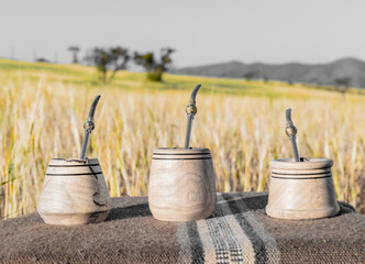 tres tazas o vasos para maté hecha en madera encima de una mesa campestre en paisaje de campo con...