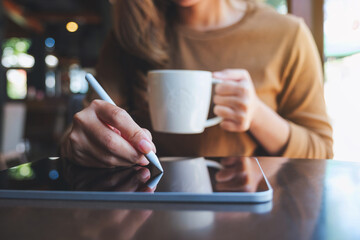 Closeup of a young woman using smart pen technology for working and writing on digital tablet screen while drinking coffee