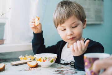 Obraz na płótnie Canvas Little boy eats a bun at the table.