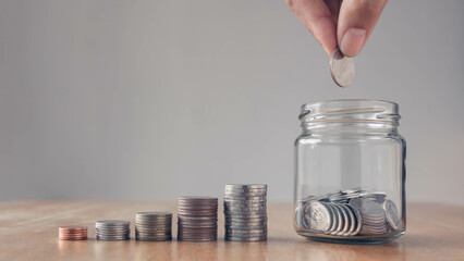 Concept of saving money for the future. Man hand putting coins in jar with money stack step growing...