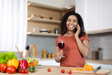 Obraz na płótnie Canvas Happy young african american woman with glass of wine calling by phone, enjoy gossip and news