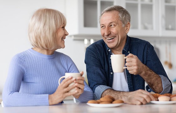 Positive elderly spouses drinking tea with pastry at home