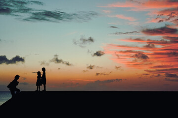 silhouette of children near the ocean at sunset
