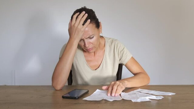 Energy bills during economic crisis. Home budget. An upset woman count on her smartphone the electricity bills for her household.
