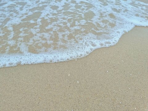 White bubbles of wave crash the sandy beach in the evening no light , for background