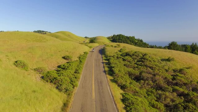 A motorcycle driving along a picturesque countryside road along green, grassy hills near Mt Tamalpais, California - aerial flyover