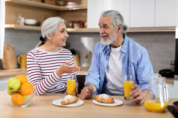 Breakfast Together. Senior Spouses Eating Croissants And Drinking Orange Juice In Kitchen