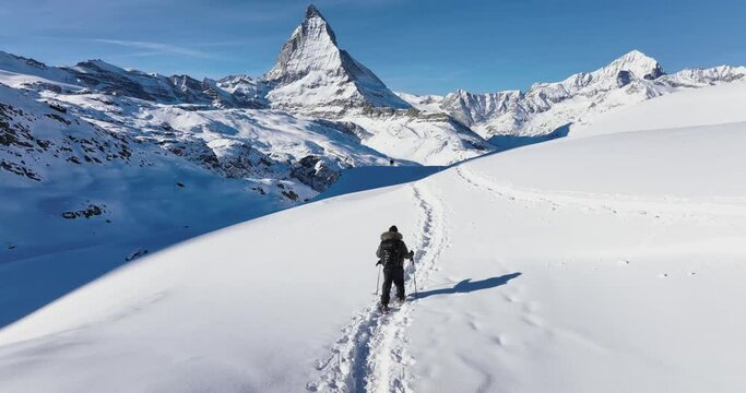 Aerial drone of Young man tourist hiker walking in snow shoes. Successful climber hiking up to mountain top swiss alps, Switzerland. Active travel lifestyle winter outdoor activities. Slow motion.