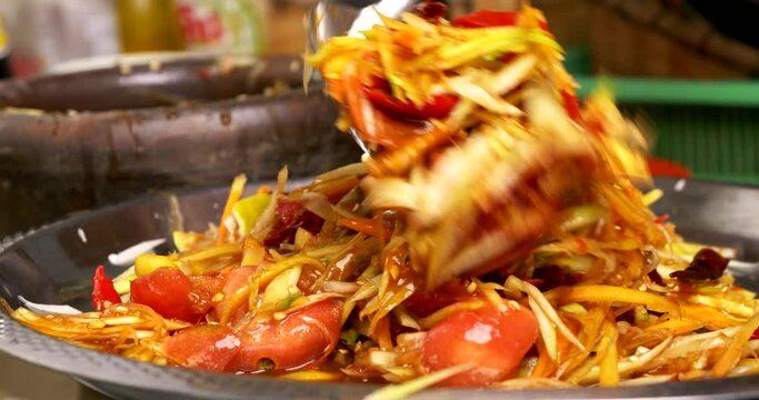 Close-up front view, Chef scooped the spicy green papaya salad or Som Tum onto the plate, Thai traditional street food. 