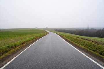 Long asphalt country road on a foggy autumn morning