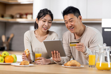 Excited asian couple shopping from home while having breakfast