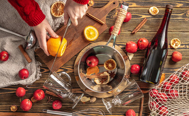 Woman is cutting oranges with a knife to cook mulled wine. Process of making a warming traditional drink, a cozy festive atmosphere
