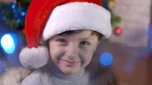 Portrait of a child at Christmas. An alone happy little girl make smiling faces by the Christmas tree in the room.