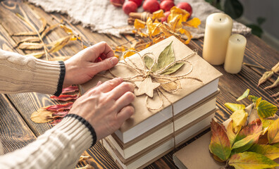 Naklejka na ściany i meble Hands of woman are carefully decorating a stack of books with craft paper covers with rope and leaves. Concept of books for a gift, autumn reading and book choice
