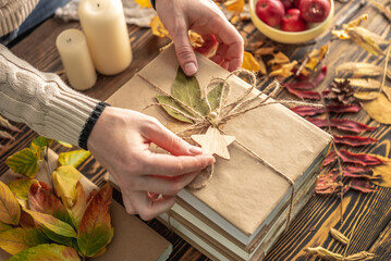 Hands of woman are carefully decorating a stack of books with craft paper covers with rope and leaves. Concept of books for a gift, autumn reading and book choice