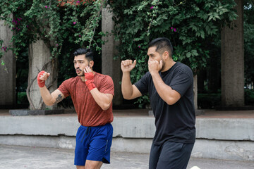 Two muscular Latino men boxing in a park, working out. Lifestyle.