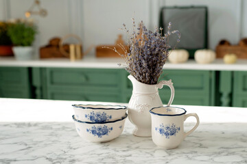 A bouquet of lavender and a set of white dishes: a porcelain milk jug, a coffee cup and bowls on a...