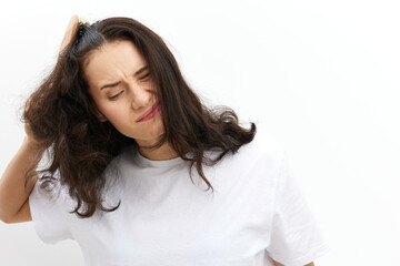 Fototapeta premium a sad, upset woman tries to comb her long, dark, tangled hair with a wooden massage comb, standing in a white T-shirt on a white background