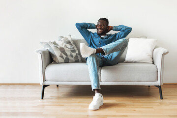 Happy Black Guy Sitting On Sofa Relaxing At Home