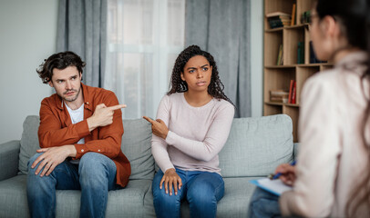 Offended sad millennial black female pointing finger at european man on meeting with psychologist
