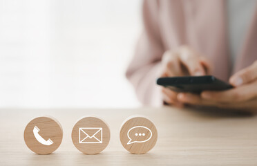 closeup phone, chat, mail icon on round wooden piece with woman using smart phone on background