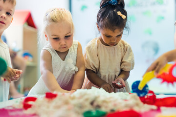 Relaxing sensory play with moldable kinetic sand at nursery school. Toddlers having fun around the...