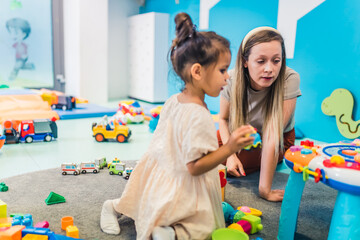 Playtime at nursery school. Toddler girl with her teacher playing with colorful educational sensory toys. Interaction with others, critical lifelong skills development, decision-making practice. High