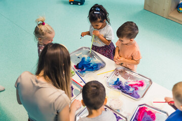 Multicultural group of children at the nursery school. Ethnic little girl milk painting, using...