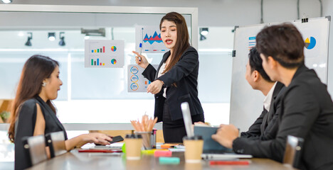 Closeup shot of millennial Asian young beautiful professional successful businesswoman lecturer in formal suit standing smiling holding pen presenting company information data document on glass board