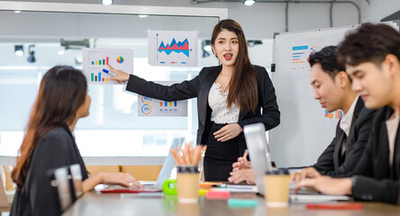 Asian young beautiful professional successful businesswoman presenter standing smiling in front of glass board after presenting while male female colleagues clapping hands thank you in meeting room