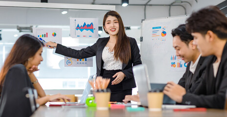 Asian young beautiful professional successful businesswoman presenter standing smiling in front of glass board after presenting while male female colleagues clapping hands thank you in meeting room