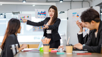 Asian young beautiful professional successful businesswoman presenter standing smiling in front of glass board after presenting while male female colleagues clapping hands thank you in meeting room