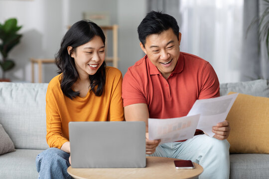 Happy asian spouses paying bills online, using laptop