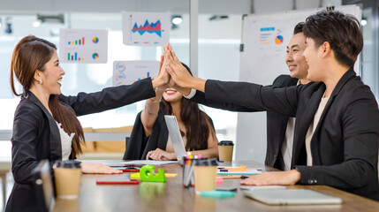 Group of millennial Asian young professional successful male businessman and female businesswoman sitting smiling holding hands high five showing unity together in office meeting room after workshop